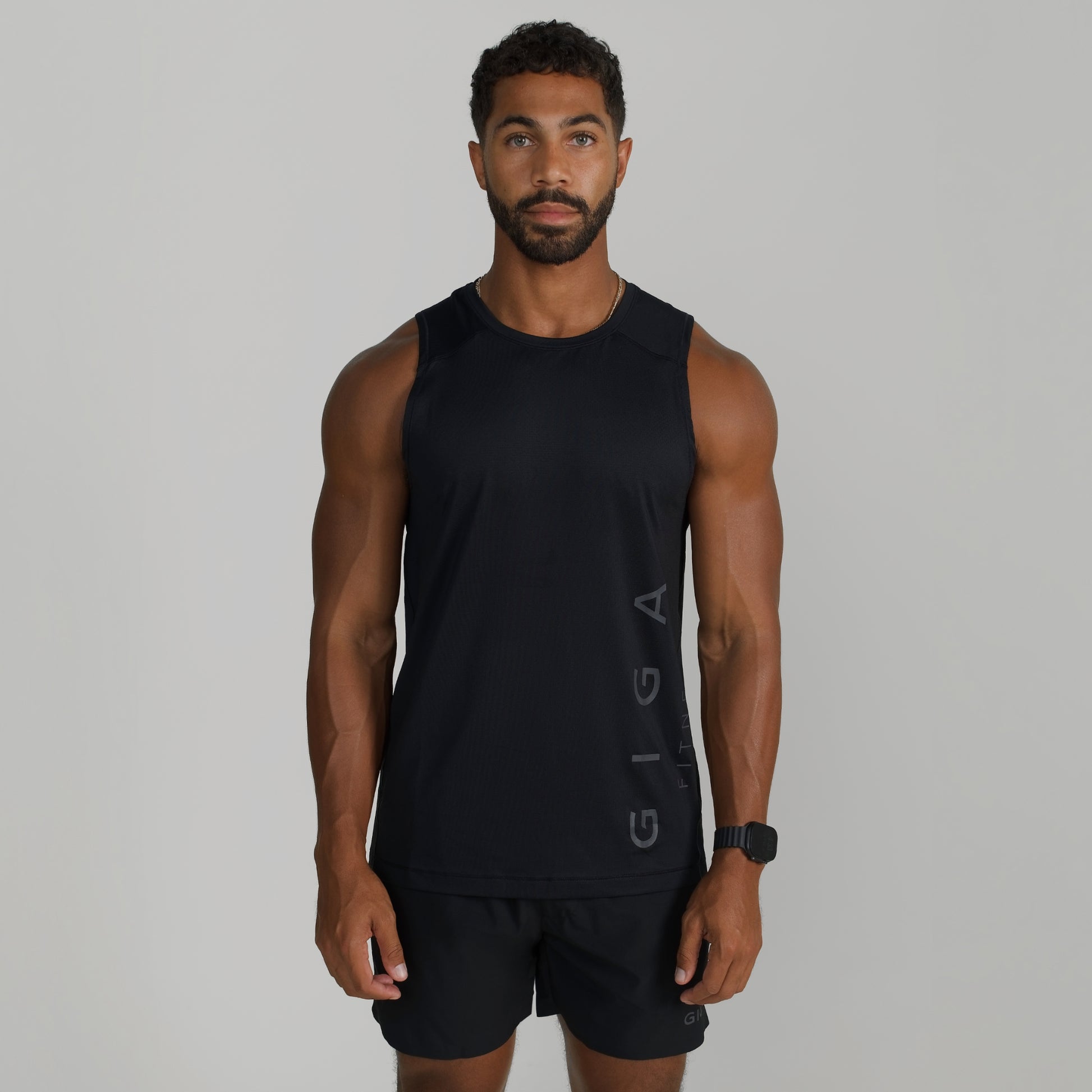 Male model wearing GIGA Core Tank in black, front view, slim fit athletic tank top