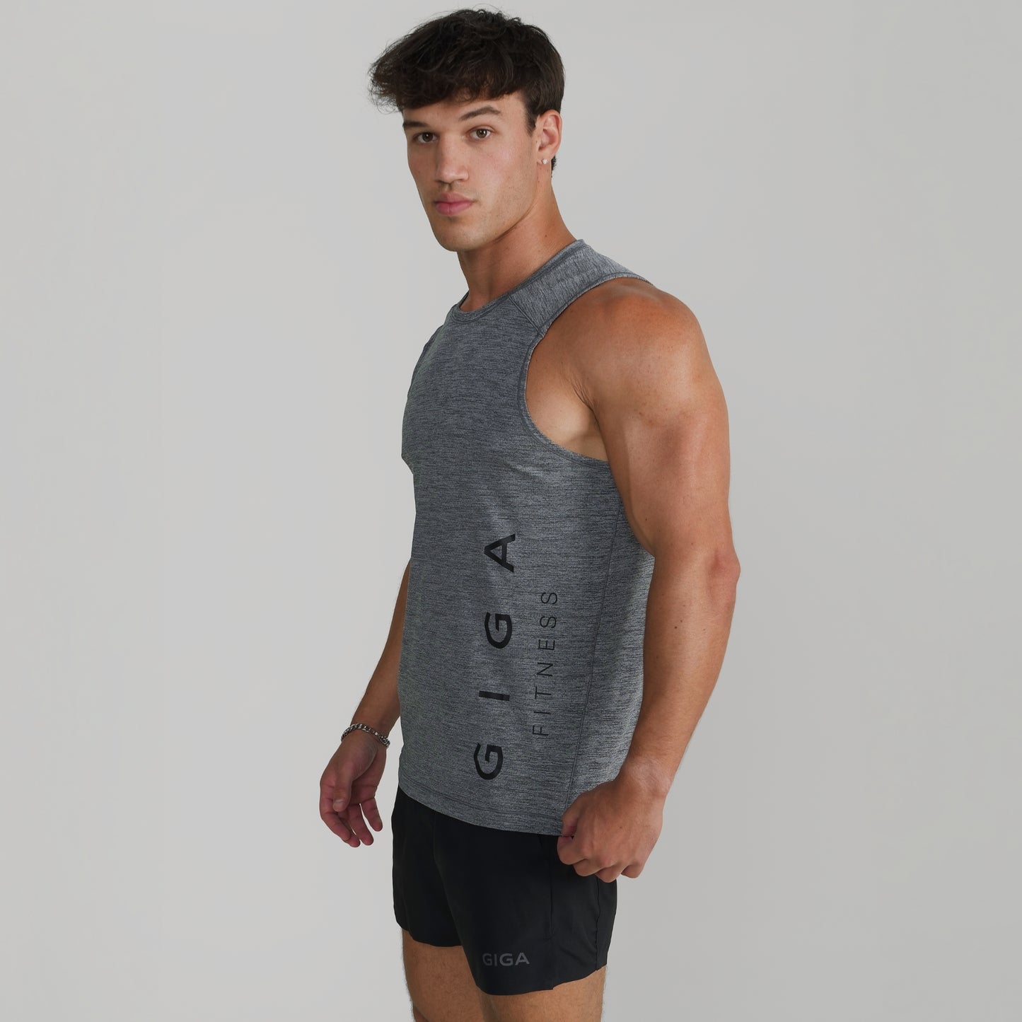 Male model wearing GIGA Core Tank in grey, side profile showing armhole and tapered fit
