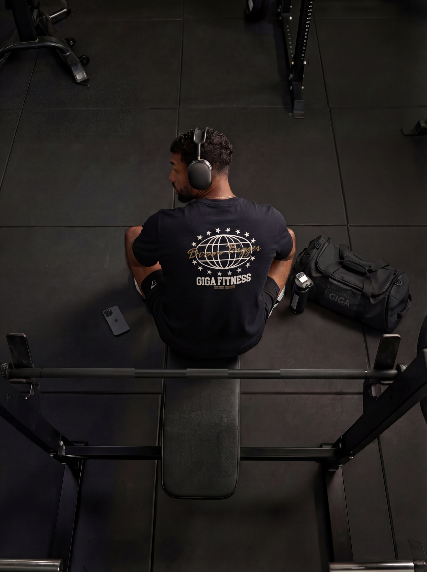Man seated at bench in gym wearing GIGA Dream Bigger Tee showing back print