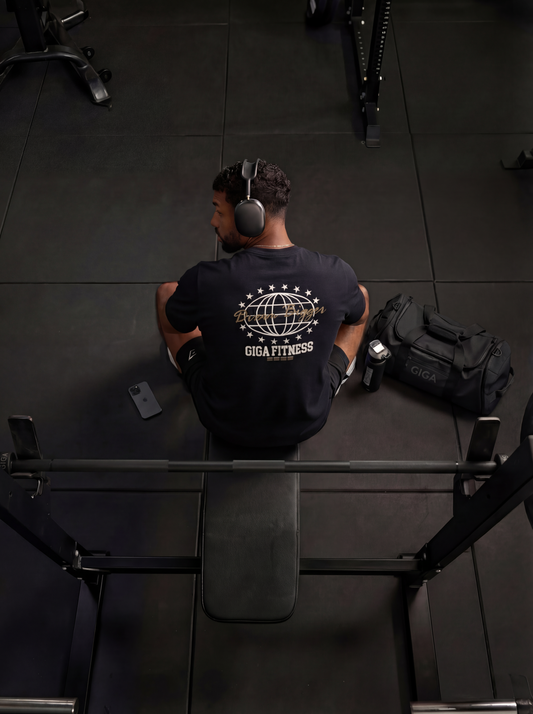 Man seated at bench in gym wearing GIGA Dream Bigger Tee showing back print