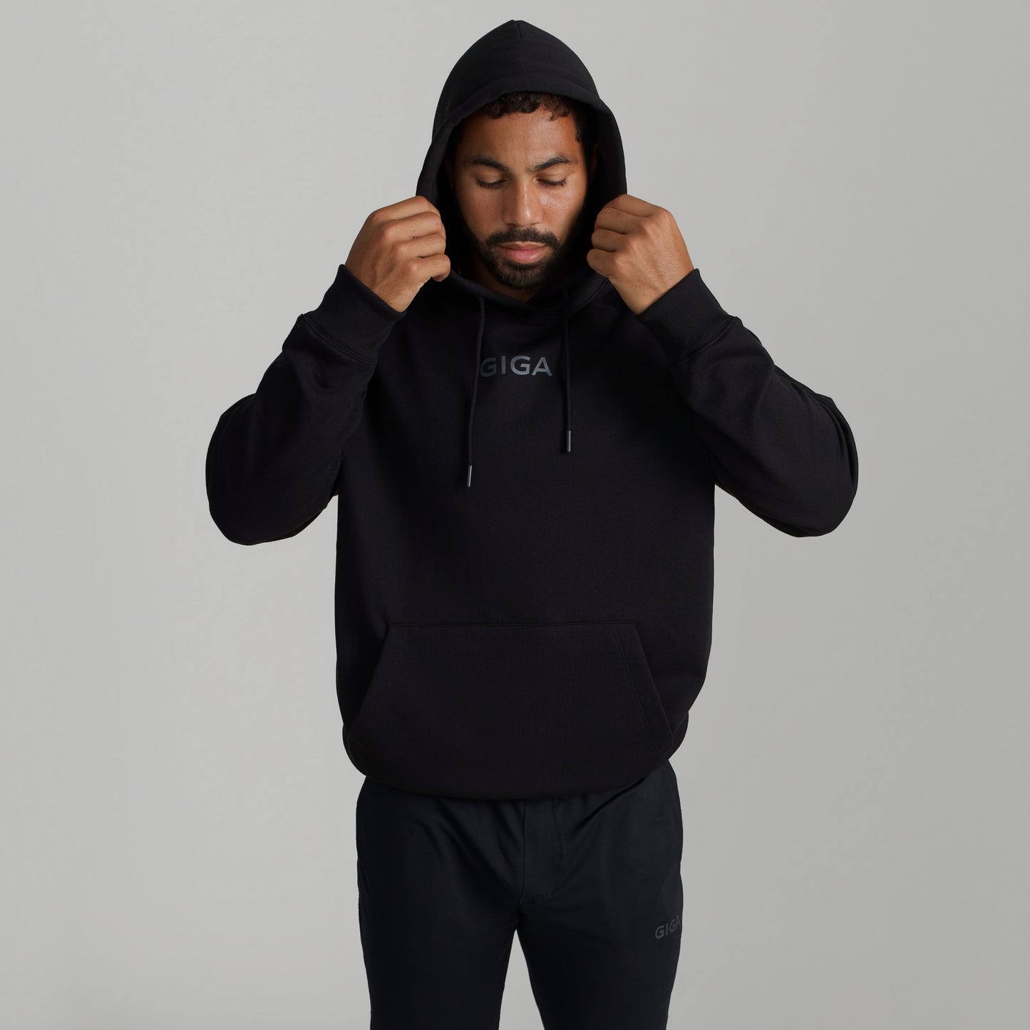 Man wearing GIGA Recovery Hoodie in black with hood up adjusting hood front view upper body