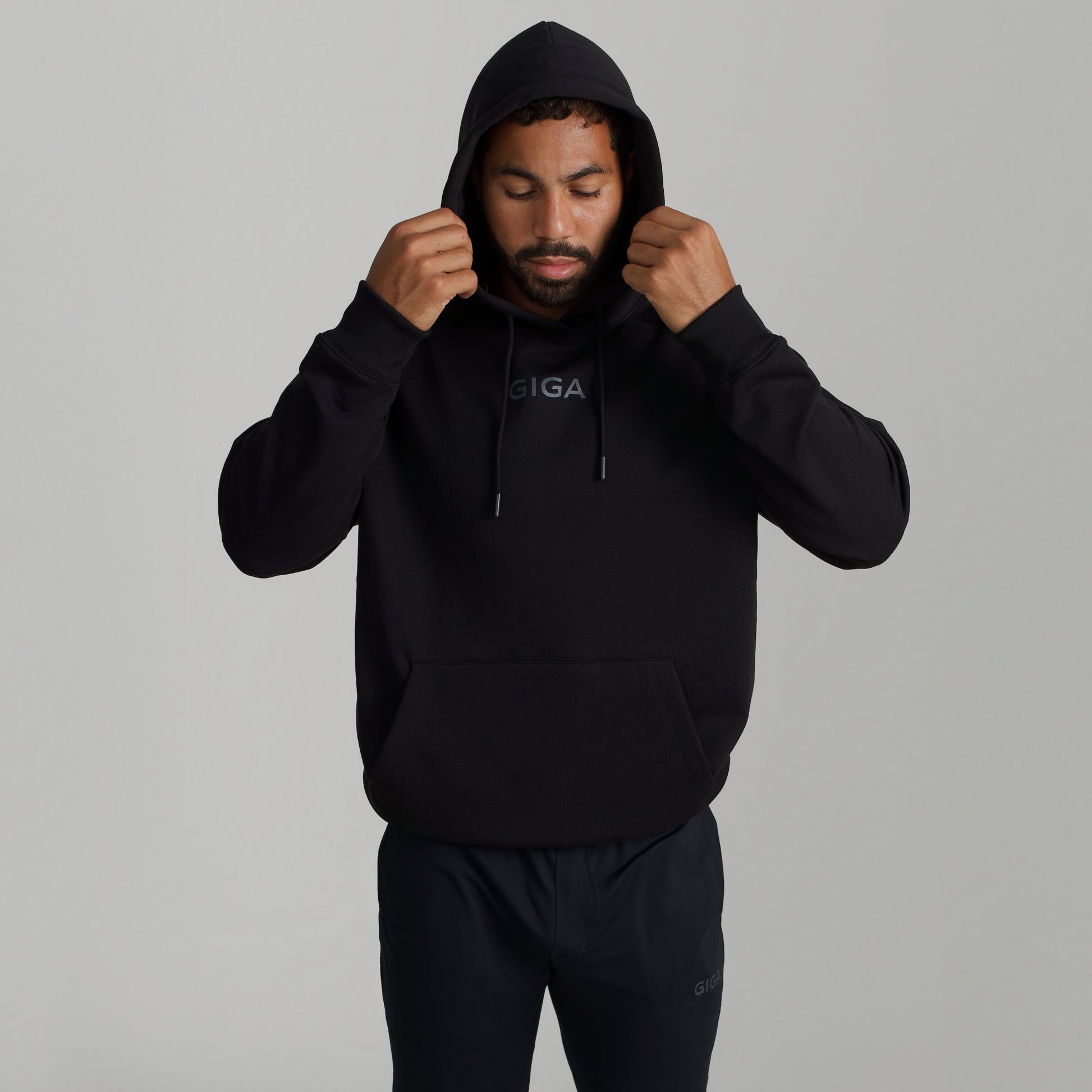 Man wearing GIGA Recovery Hoodie in black with hood up adjusting hood front view upper body